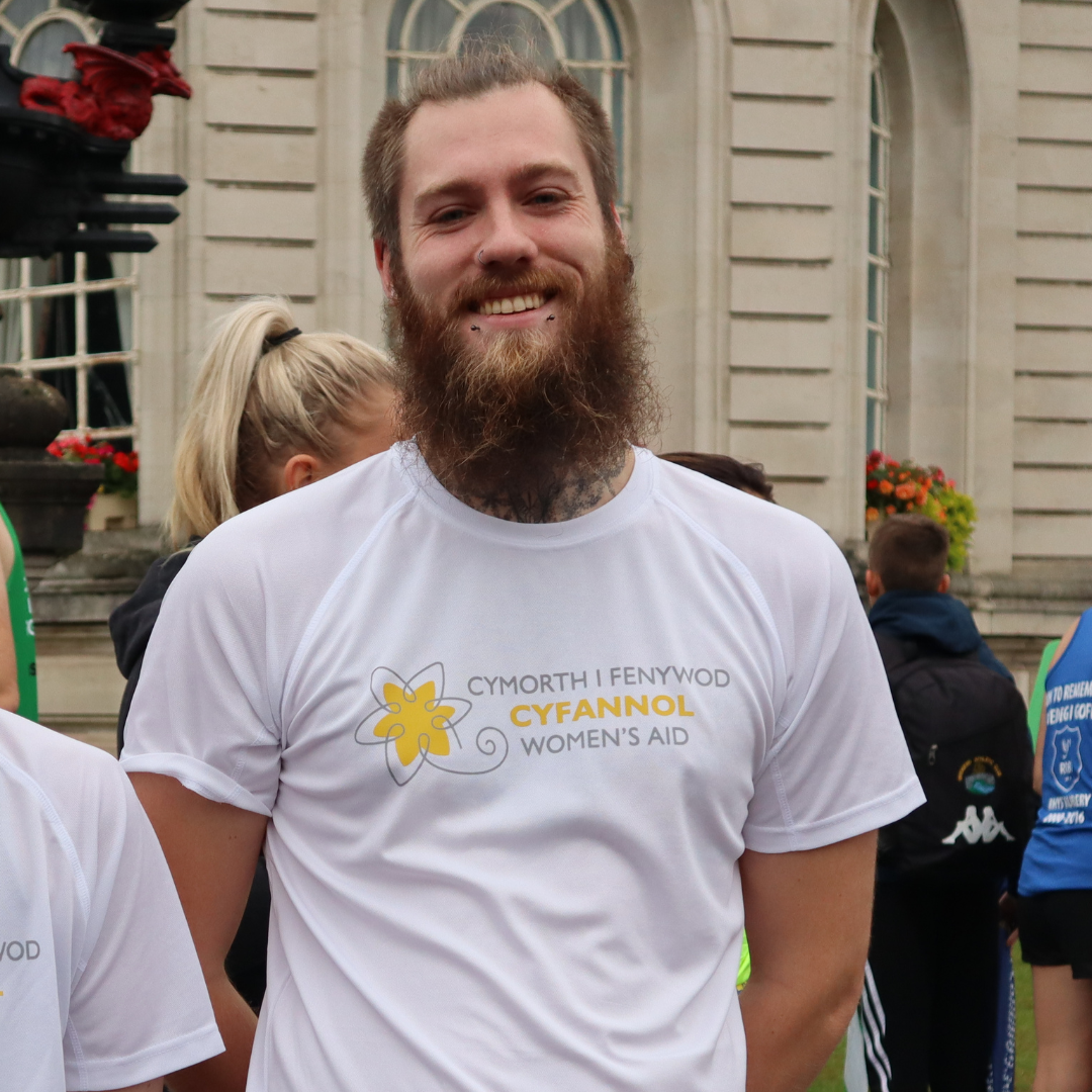 Man posting for photo smiling while wearing a Cyfannol Women's Aid t-shirt before Wizz Air Cardiff Half Marathon.