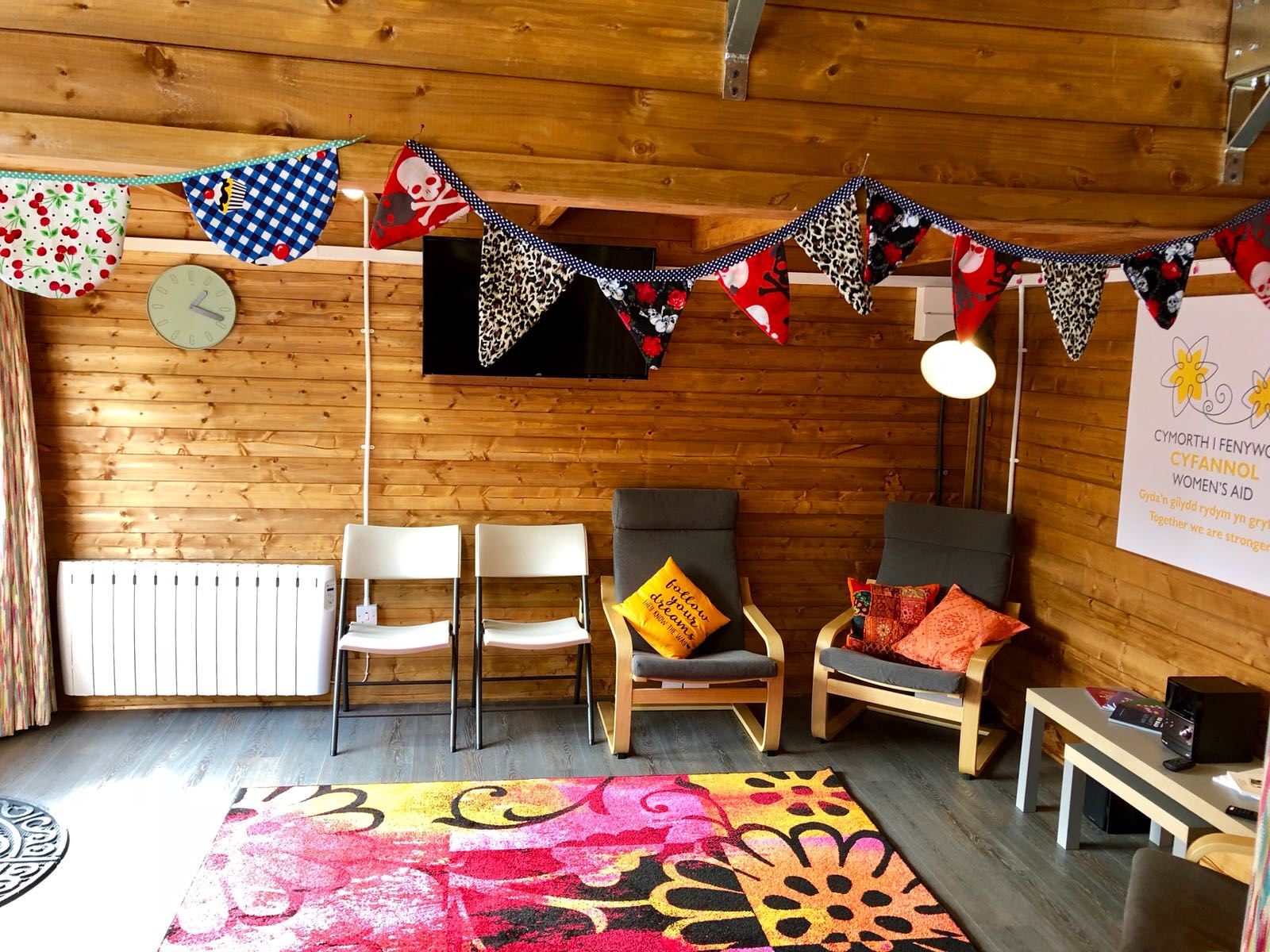 Shed with wooden walls. It's decorated with bunting, chairs and a colourful rug.