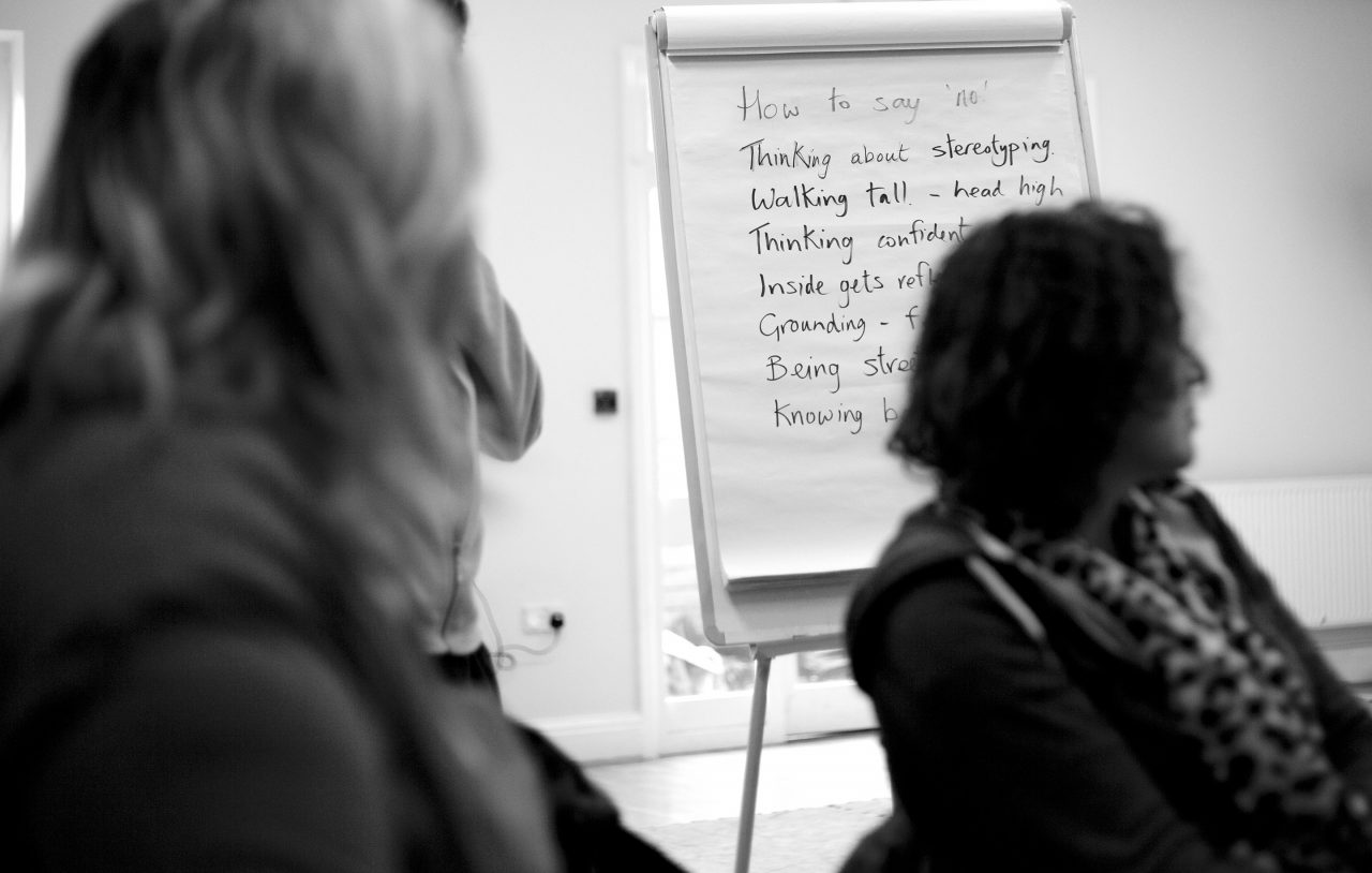Black and white shot of two people sitting in a room looking away from the camera. There is a flipchart in the background.