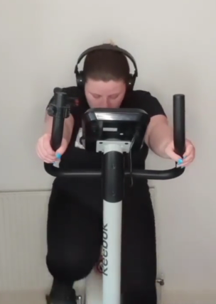 Person wearing headphones, looking down. They're on an exercise machine.