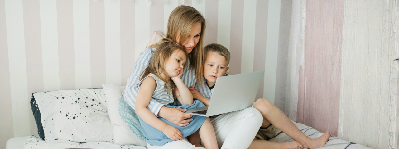 Woman and two children sat on a bed looking at laptop screen.